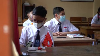 BALI, INDONESIA-5 OCT 2021: Endonezya ortaokulundaki sınıf atmosferi yeni normalliği öğrenirken. Öğrenciler sınıfta çalışırken sağlık maskesi takıyor.