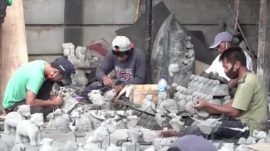 Ubud, 17 Nisan 2020: Ubud, Bali 'deki zanaatkarlar, bitirilmiş parçalarla dolu geleneksel bir atölyede ayrıntılı taş heykeller oydular