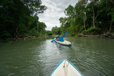Bali, 9 Aralık 2020: Taman Hutan Raya Ngurah Rai, Bali 'de yoğun yağış sonrasında yoğun tropikal ormanlarla çevrili su baskınlarında iki kişi kanoya bindi