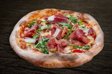 Prosciutto, roka, kapari, pelati soslu Sorrentina pizzası, pesto. Ahşap arka planda Napolili yuvarlak pizza.