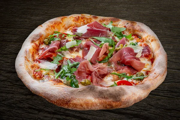 Sorrentina pizza with prosciutto, arugula, capers, pelati sauce, pesto. Neapolitan round pizza on wood background