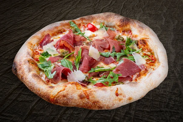 Sorrentina pizza with prosciutto, arugula, capers, pelati sauce, pesto. Neapolitan round pizza on wood background