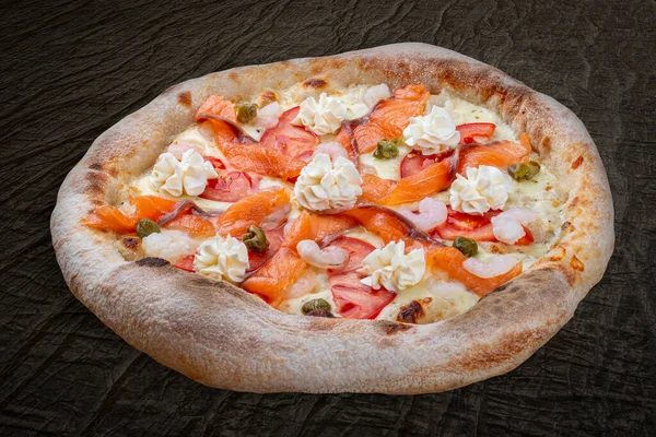 Philadelphia pizza with salmon, shrimps, tomatoes, mozzarella, capers, Philadelphia cheese. Neapolitan round pizza on wood background
