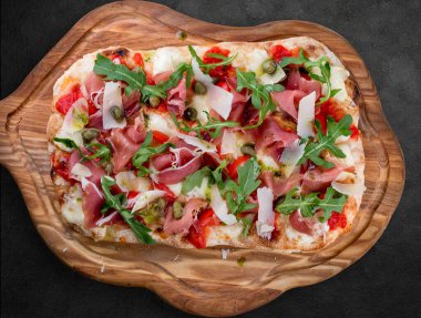 Prosciutto, roka, kapari, pelati soslu Sorrentina pizzası, pesto. Koyu arkaplanda Roma pizzası dikdörtgeni