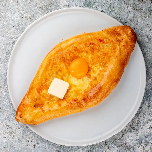 Peynirli, yumurtalı ve tereyağlı Adjar tarzı khachapuri. Kafkas mutfağı. Gri arkaplandaki izole görüntü.