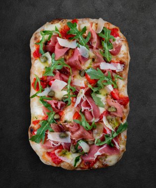 Prosciutto, roka, kapari, pelati soslu Sorrentina pizzası, pesto. Koyu arkaplanda Roma pizzası dikdörtgeni