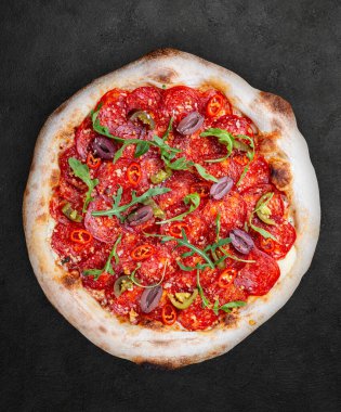 Chorizo, roka, jalapeno, chili, kalamata, pesto soslu pizza. Koyu arkaplanda Napolitan yuvarlak pizza