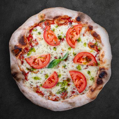 Domatesli pizza, mozzarella, pesto sosu, fesleğen. Koyu arkaplanda Napolitan yuvarlak pizza