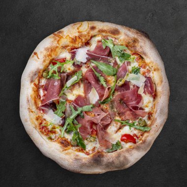 Prosciutto, roka, kapari, pelati soslu Sorrentina pizzası, pesto. Koyu arkaplanda Napolitan yuvarlak pizza