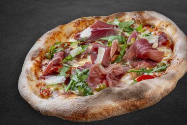Prosciutto, roka, kapari, pelati soslu Sorrentina pizzası, pesto. Koyu arkaplanda Napolitan yuvarlak pizza