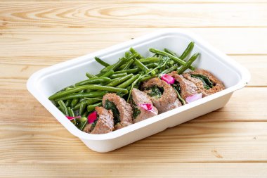 Ispanaklı dana sarması ve kuşkonmaz fasulyesi. Sağlıklı beslenme. Paket yemek. Çevre ambalajı. Ahşap bir arka planda.