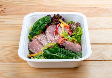 Biftek soslu salata. Sağlıklı yiyecekler. Paket yemek. Ahşap bir arka planda.