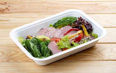 Biftek soslu salata. Sağlıklı yiyecekler. Paket yemek. Ahşap bir arka planda.
