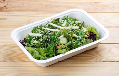 Chuka yosunlu Hakkaido salatası, sulu elma ve fındık sosu. Sağlıklı yiyecekler. Paket yemek. Ahşap bir arka planda.