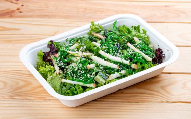 Chuka yosunlu Hakkaido salatası, sulu elma ve fındık sosu. Sağlıklı yiyecekler. Paket yemek. Ahşap bir arka planda.