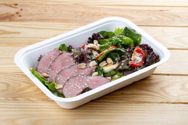 Biftek soslu salata. Sağlıklı yiyecekler. Paket yemek. Ahşap bir arka planda.