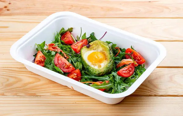 Avokadoda fırında yumurta, marul ve domates. Sağlıklı beslenme. Paket yemek. Ahşap bir arka planda.
