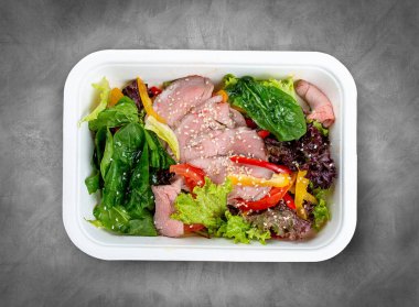 Biftek soslu salata. Sağlıklı yiyecekler. Paket yemek. Üst görünüm, gri arkaplanda.