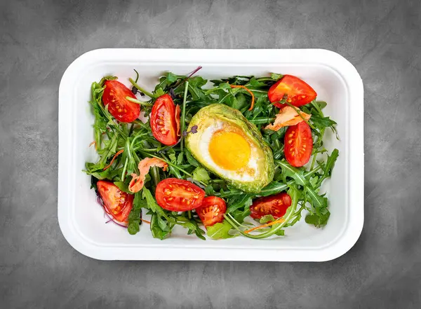 Avokadoda fırında yumurta, marul ve domates. Sağlıklı beslenme. Paket yemek. Üst görünüm, gri arkaplanda.