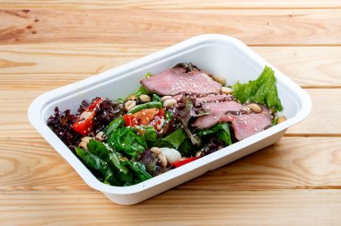 Biftek soslu salata. Sağlıklı yiyecekler. Paket yemek. Ahşap bir arka planda.