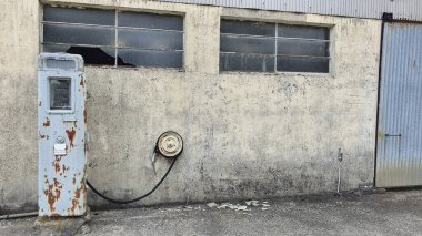 Orada kimse yaşamıyormuş gibi görünen bir çiftlik evinin önünde terk edilmiş eski bir benzin pompası. Binanın camları kırılmış ve pompanın metali paslanmış ve ağır hasar görmüş..