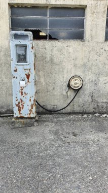 Orada kimse yaşamıyormuş gibi görünen bir çiftlik evinin önünde terk edilmiş eski bir benzin pompası. Binanın camları kırılmış ve pompanın metali paslanmış ve ağır hasar görmüş..