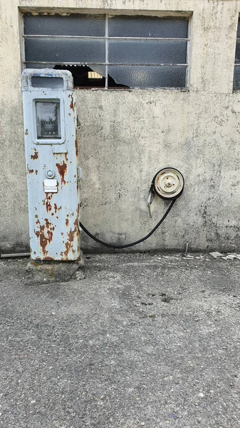 Orada kimse yaşamıyormuş gibi görünen bir çiftlik evinin önünde terk edilmiş eski bir benzin pompası. Binanın camları kırılmış ve pompanın metali paslanmış ve ağır hasar görmüş..