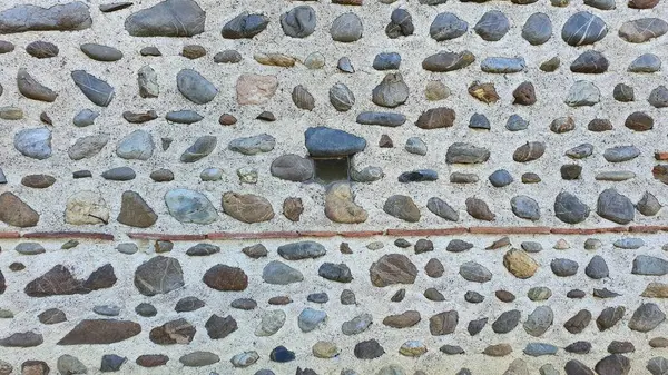 Concrete wall with embedded river stones and a tiny window in the middle of it