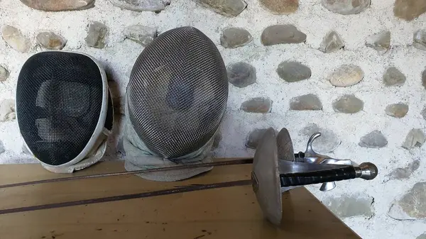 Antique fencing mask and swords on a wooden cabinet and a stone wall