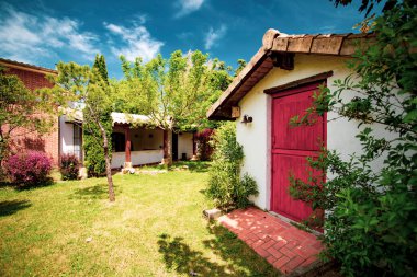 Kırmızı kapısı olan küçük beyaz bir kulübe ve girişte yeşil ışıklar ve yaz günü beyaz bulutlarla çevrili mavi gökyüzü..