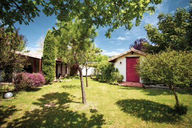 Kırmızı kapısı olan küçük beyaz bir kulübe ve girişte yeşil ışıklar ve yaz günü beyaz bulutlarla çevrili mavi gökyüzü..