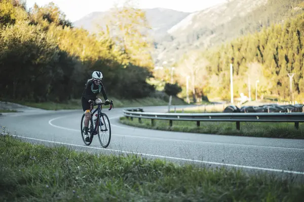 stock image A woman cyclist training on a lonely road on a sunny day wearing a black jersey and bib shorts and a white helmet. 