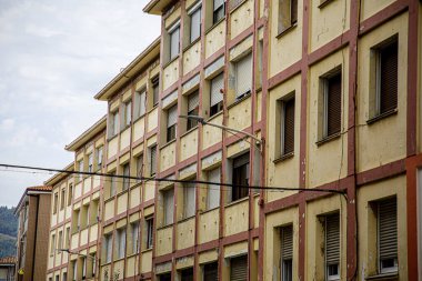 Görüntü, değişken tuğla ve beyaz beton duvarlarla karakterize edilmiş klasik, rustik görünümlü çok katlı bir konut binasını gösteriyor. Yapı, birden fazla penceresi eşit aralıklarla aralıklı olan kentsel ya da banliyö mahallesine özgü bir yapıdır.