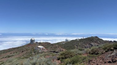 Two observatories sit high above the clouds on a rugged mountain, offering a breathtaking view of the sky and horizon, ideal for astronomical observation and scientific research. clipart