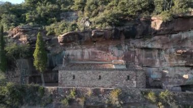 Ermita de lAbellera 'yı bir dron yakalar, kayalıkların içine inşa edilmiş küçük bir taş inziva yeri, verimli orman ve kayalık manzaralarla çevrili, sakin ve gizli bir ortamda doğayla kusursuz bir şekilde harmanlanmış..