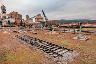 Abandoned Railroad Track in Industrial Landscape. A desolate railway track with a crane and industrial factory in the background. Captured on a cloudy day, evoking a sense of abandonment and nostalgia. clipart