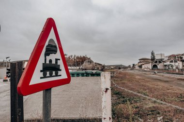 Kırsal İstasyonda Demiryolu Geçidi İşareti. Bulutlu bir günde arka planda kırsal ve kırsal bir istasyon olan üçgen demiryolu geçidi işaretinin yakın çekimi ihtiyatı ve nostaljiyi çağrıştırıyor..