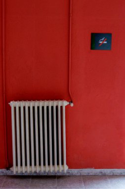 Kızıl Duvar 'a karşı radyatör ve Sigara İçilmez işareti. Beyaz bir radyatörün kırmızı bir duvara dayandığı minimalist kompozisyon üzerinde küçük bir 