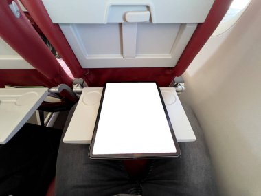 Ekonomi sınıfındaki yolcumuz tepside tablet kullanıyor. Uçak koltuğu, modern hava yolculuğu konforu ve teknolojisini yansıtan bir eğlence ekranı ve pencere manzarasına sahip..