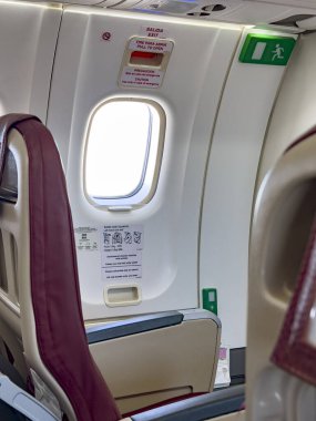 Interior of an airplane showing an emergency exit row seat with a window. Safety instructions and exit signs are visible, highlighting air travel security and cabin design clipart