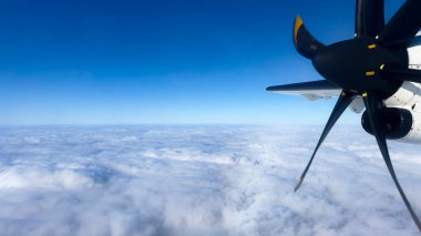 Aerial view from a turboprop airplane flying above the clouds. The spinning propeller, blue sky, and fluffy clouds create a stunning perspective of air travel and aviation clipart