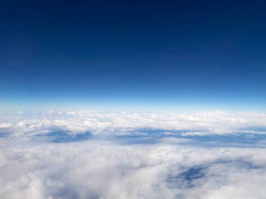 Derin mavi bir gökyüzünün altında ufka uzanan beyaz bulutların geniş hava manzarası. Yüksek irtifa perspektifi, hava yolculuğunun ve doğanın güzelliğini yakalar..
