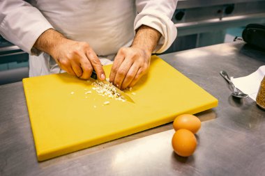 Close-up of a chef finely chopping ingredients on a yellow cutting board in a professional kitchen. Precision knife skills are key to culinary expertise and food preparation. clipart