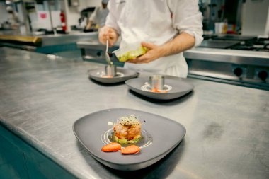Profesyonel şef bir restoranın mutfağında bir gurme tabağını dikkatlice kaplıyor. Taze malzemeli, hassas ve sanatsal sunumlu kaliteli yemekler.