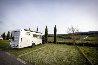 Güzel bir kırsal alanda çimenli bir arazide park etmiş beyaz bir karavan..