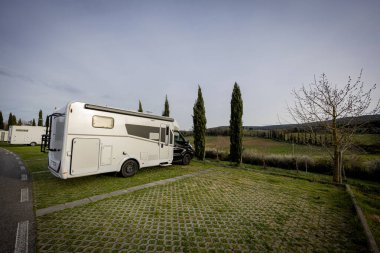 Güzel bir kırsal alanda çimenli bir arazide park etmiş beyaz bir karavan..