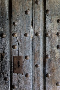 Eski yıpranmış ahşap bir kapıya yakın çekim. Süslü paslı metal kilidi ve desenli tahılları var. Kaliteli, kırsal ayrıntı güçlü karakter ve patinaj ile.