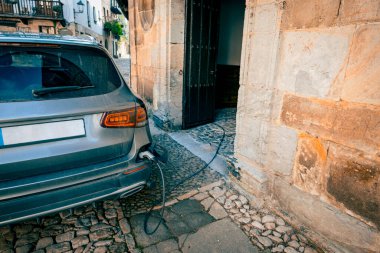 Tarihi bir taş bina tarafından şarj edilen modern elektrikli araç, eski dünya mimarisi ile bir kaldırım taşı kasabasında sürdürülebilirliği harmanlıyor..