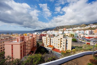 La Palma 'da canlı binaları, dağ zeminleri ve dramatik bulutlar altında Atlantik Okyanusu olan bir sahil kasabasının panoramik manzarası yükseldi..