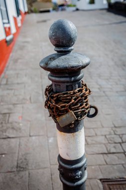 Aşınmış zincir ve asma kilide sarılı eski metal bir direğe yakın çekim, sınırlama, kontrol ve psikolojik kısıtlama hissi uyandırıyor..